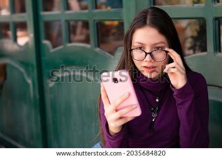 Girl with glasses a little surprised looking at her cell phone while waiting in a latino alley