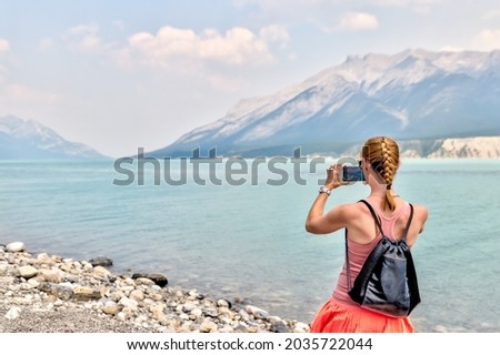 Blonde athletic woman taking pictures on the shores of Abraham Lake in the Canadian Rocky Mountains