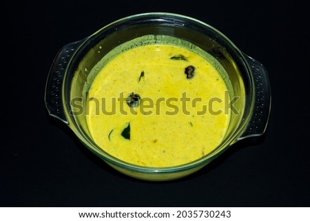Closeup Image Of Kerala Onam Special Traditional Yellow Buttermilk Curry Also Known As Moru Curry, Pulissery, Kachiya Moru In Glass Bowl. Black Background