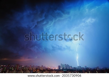 Amazing view of the night storm over the big city, with colorful clouds moving on the sky and bringing first drops of rain, and bright lightnings illuminating the scene.