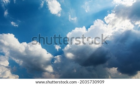 Amazing view of white fluffy clouds moving softly on bright blue sky. Beautiful sun rays shine through the clouds creating peaceful atmosphere which gradually changes to stormy one.