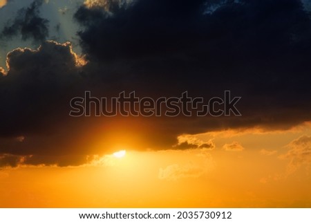The sun is going down among the clouds. Close up view to the sunset and picturesque clouds of bright orange and yellow colors.