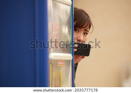 A woman taking a picture with a smartphone from behind a vending machine 