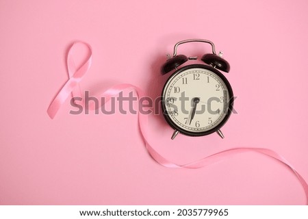 Don't miss the time, flat lay composition with an alarm clock and a pink ribbon. Breast Cancer Awareness, medical concept isolated on pink background with copy space.