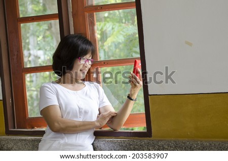 the cute middle aged Asian woman smile and take photography with mobile phone