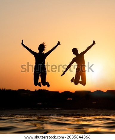 Happy friends are having fun and jump at sunset beach in sunlight.