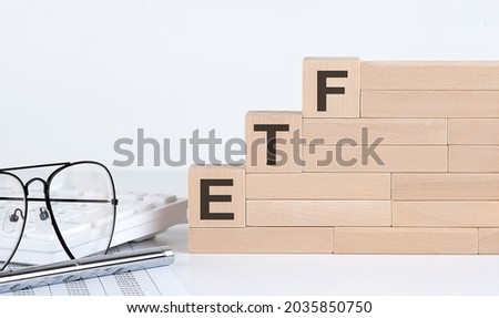 wooden cubes with letters ETF on white table with keyboard and glasses