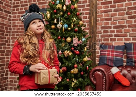 Cute funny girl holds a gift box and smiles happily. Beautiful Christmas tree in the background. Christmas and New Year. 