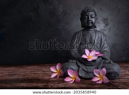 Buddha statue with frangipani flowers on a dark background