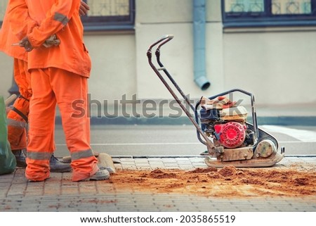 Vibrating plate on construction site. Compaction sand into paving slabs. Grout paving slabs. Plate compactor for compaction soil or pavement on sidewalk Royalty-Free Stock Photo #2035865519