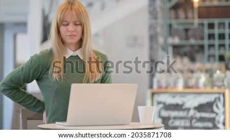 Woman having Back Pain while using Laptop in Cafe 