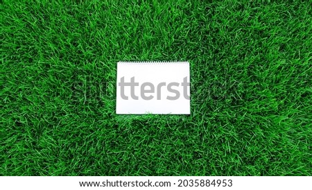 Mock-up empty white paper on green grass background. Сard on nature for message flat lay with copy space for text or products presentation. Nature concept, business and lifestyle environment. Top view