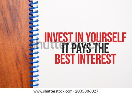Text Invest in Yourself It pays the best interest written in notepad, Office wood table from above, concept image for blog title or header image. Aged vintage color look.