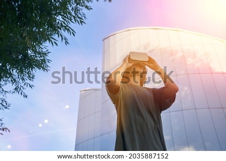 A girl is having fun in virtual reality glasses, standing against the background of a mirrored building. The concept of the future. High-quality photo