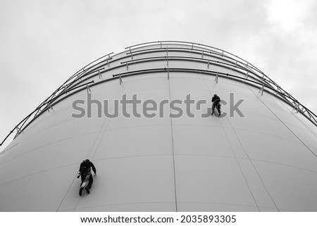Picture monochrome male two workers control rope down top roof height tank rope access inspection of thickness shell plate storage tank gas safety work at height.