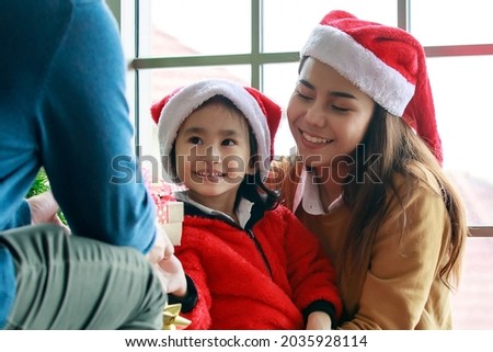 Happy Asian family daughter girl sit on mother lap smiling exciting surprising together when receiving present gift boxes from father in Christmas eve celebration evening in living room at home.