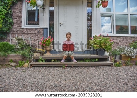 a girl child with a laptop is sitting on the porch of the house during a lesson on a remote photo without a filter