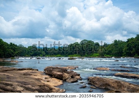 River Flows Between Rocks In Rainforest under blue cloudy sky Chalakudy Kerala