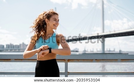 Uses a smart watch to measure the pulse on the hands. A woman does sports on the street. Fitness and a healthy lifestyle. The trainer does exercises for stretching the body.