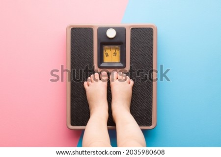Baby barefoot standing on weight scales on light pink blue floor background. Pastel color. Closeup. Care about body. Children weight control concept. Royalty-Free Stock Photo #2035980608
