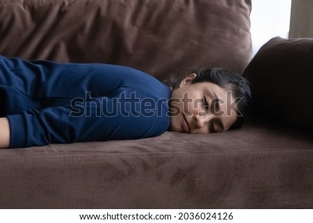 Close up exhausted Indian woman falling asleep after long workday, lying on couch, tired young female with closed eyes resting on sofa, taking nap, daydreaming, fatigue and lack of energy concept Royalty-Free Stock Photo #2036024126