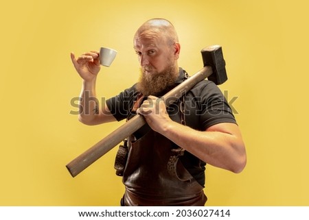 Coffee break. Comic image of bearded bald man, blacksmith leather apron or uniform isolated on yellow background. Concept of labor, retro professions, power, beauty, humor. Funny meme emotion