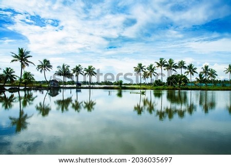Palm trees and small huts reflections, Kerala backwaters photography during day time Kadamakkudy Kerala, Stripe of coconut trees between a cloudy sky and river. Royalty-Free Stock Photo #2036035697