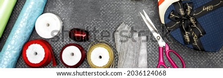 Christmas background with gift boxes, clews of rope, paper's rolls and colorful ribbons and scissor on leather gray background. Preparation for holidays. Top view with copy space