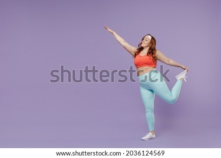 Full length side view young chubby overweight plus size big fat fit woman wear red top warm up training do legs stretch exercise isolated on purple background gym. Workout sport motivation concept.