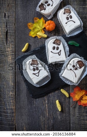 Homemade baked halloween party. Funny cookies in white chocolate glaze ghost on a wooden table. Top view flat lay background. Copy space.