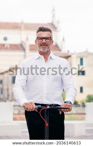 Handsome businessman in suit riding an electric scooter while commuting to work in the city. Ecological transport concept Royalty-Free Stock Photo #2036140613