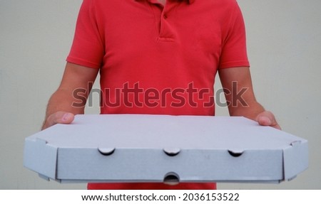 Pizza delivery. A courier in a red polo holds a cardboard box with pizza. Food delivery