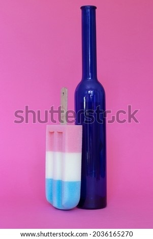 Beautiful blue glass bottle with colorful ice cream against pastel pink background. Side view. Minimal composition.