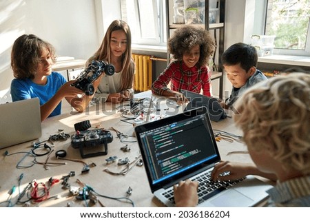Diverse school children students build robotic cars using computers and coding. Happy multiethnic kids learning programming robot vehicles sitting at table at STEM education science engineering class. Royalty-Free Stock Photo #2036186204