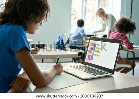 Smart teen kid boy junior middle school student using laptop learning coding data computer science digital software program information technology sitting at desk during class studying in classroom. Royalty-Free Stock Photo #2036186207