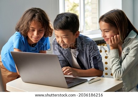 Diverse happy school kids using laptop computer together in classroom. Multicultural children junior students classmates learning online elementary education program class gathered at desk. Royalty-Free Stock Photo #2036186216