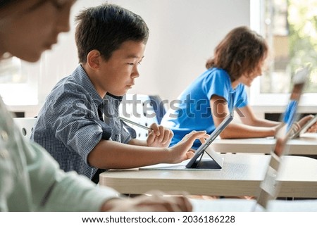 Focused Asian school boy using digital tablet at class in classroom. Attentive junior school student learning online virtual education digital program app tech during stem computer science lesson. Royalty-Free Stock Photo #2036186228