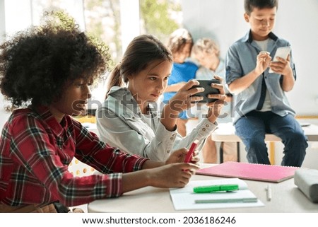 Diverse multiethnic kids students using smartphones in classroom. Multicultural children holding devices having fun with mobile phones apps playing games and checking social media at school. Royalty-Free Stock Photo #2036186246