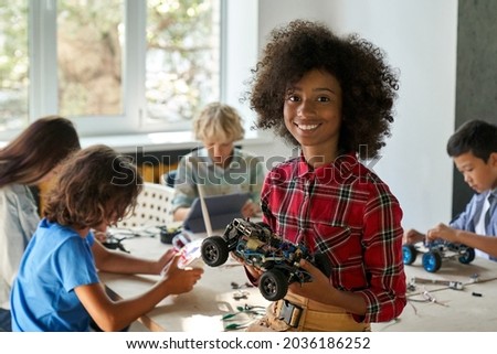 Happy African American junior school kid holding robotic car looking at camera at STEM class. Smiling black child preteen girl posing with robot vehicle. Portrait. Engineering and coding education. Royalty-Free Stock Photo #2036186252