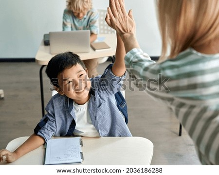 Happy Asian kid boy giving high five to female teacher at class in classroom. Teacher encouraging cheerful chinese helping child student giving support during elementary junior school lesson. Royalty-Free Stock Photo #2036186288