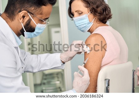 Older woman wearing face mask getting vaccination injection. Indian doctor vaccinating old patient. Vaccine and senior people inoculation, elderly immunity for covid prevention immunization concept. Royalty-Free Stock Photo #2036186324
