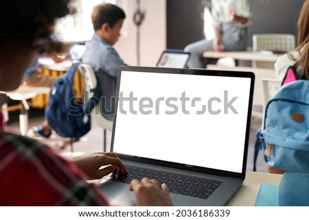 African junior school kid girl student using laptop computer with white blank empty mockup screen at desk in classroom. Online education class software website tech ads concept. Over shoulder view Royalty-Free Stock Photo #2036186339