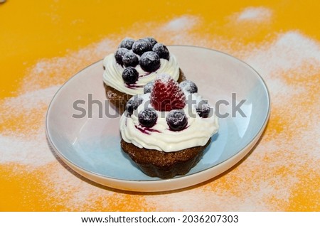 homemade cupcake, cupcake sprinkled with blueberry powder with strawberries, cream cake sprinkled with chocolate, on an orange background. selective focus
