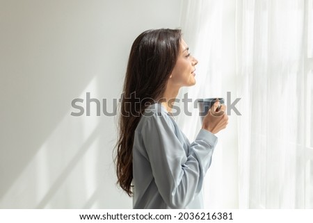 Happy woman stand drink coffee and opening window curtains breathe fresh air stretch exercise in bedroom. Female overjoyed welcome new life at new home. Optimism and mental health concept Royalty-Free Stock Photo #2036216381