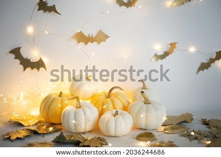 Sweet mini pumpkins, golden autumn leaves and bats on a white wooden table with copy space. Halloween decor.