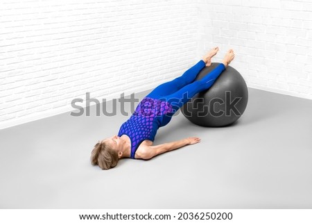 Reverse plank with exercise ball. Caucasian slim woman in blue sportswear does workout in fitness studio indoor, high angle view.