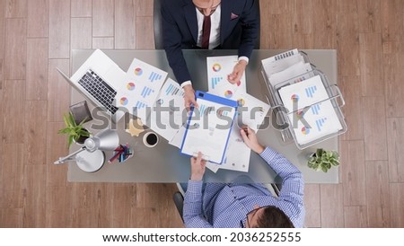 Top view of businessman signing business contract after analyzing company documents while discussing investments during partnership. Businessmen working at company strategy in startup office