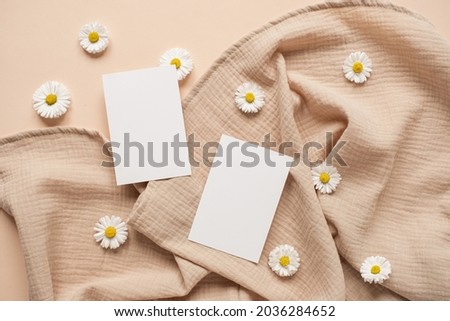 Blank clipping path paper sheet card with mockup copy space, chamomile flower buds and muslin cloth on neutral beige background. Minimal aesthetic business brand template. Flat lay, top view