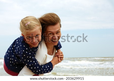 happy mother and daughter cuddling on the beach near the ocean coast in summer