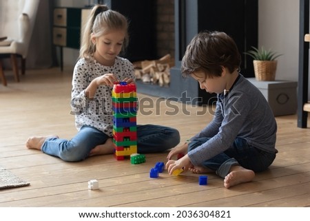 Two cute sibling children completing tower model form plastic building blocks. Boy and girl playing learning games, sitting on heating floor at home together. Safe comfortable house concept Royalty-Free Stock Photo #2036304821